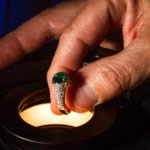 A modern 18K gold emerald and diamond ring being examined prior to appraisal.